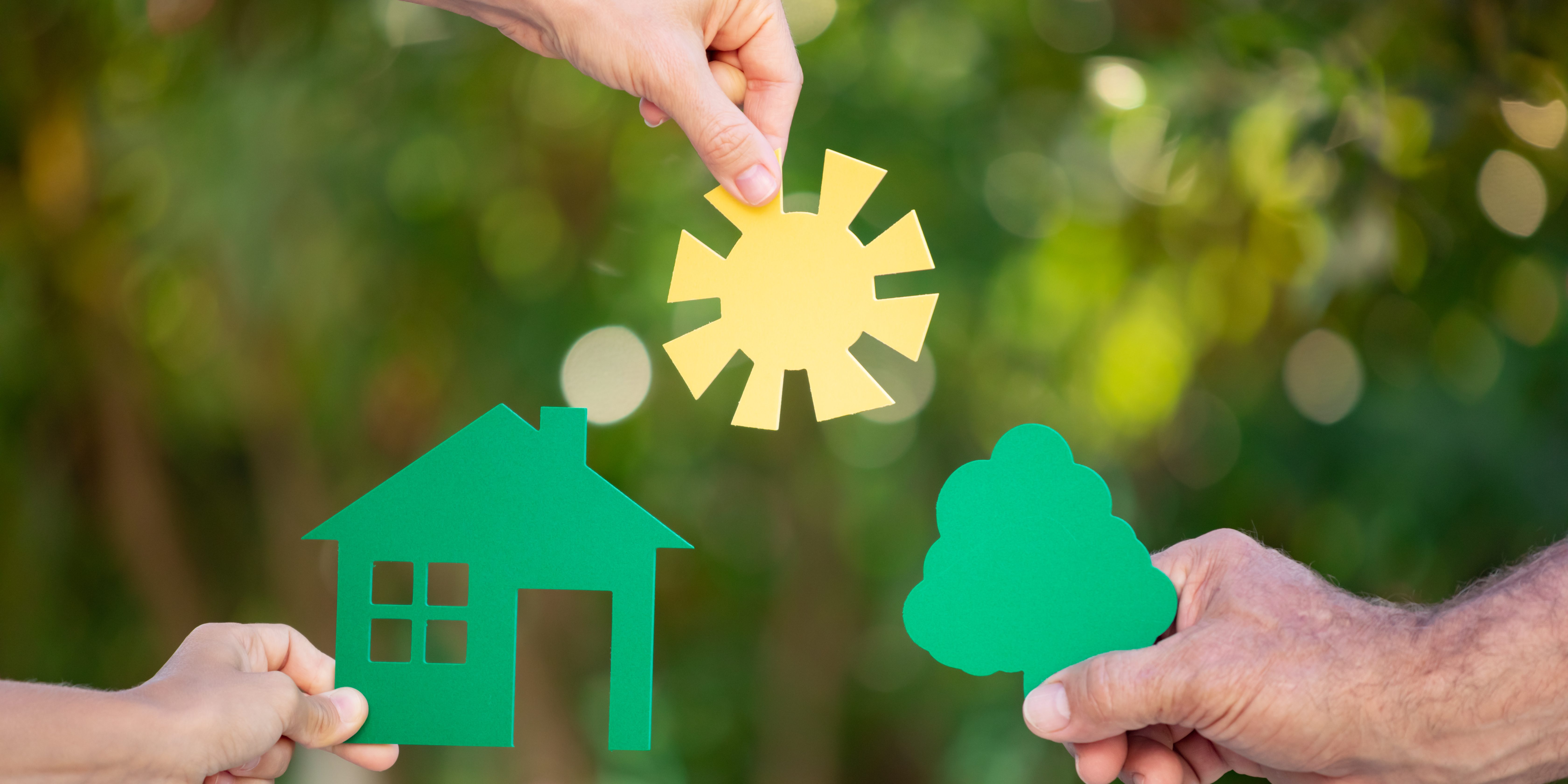 Family holding house in hands against spring green background