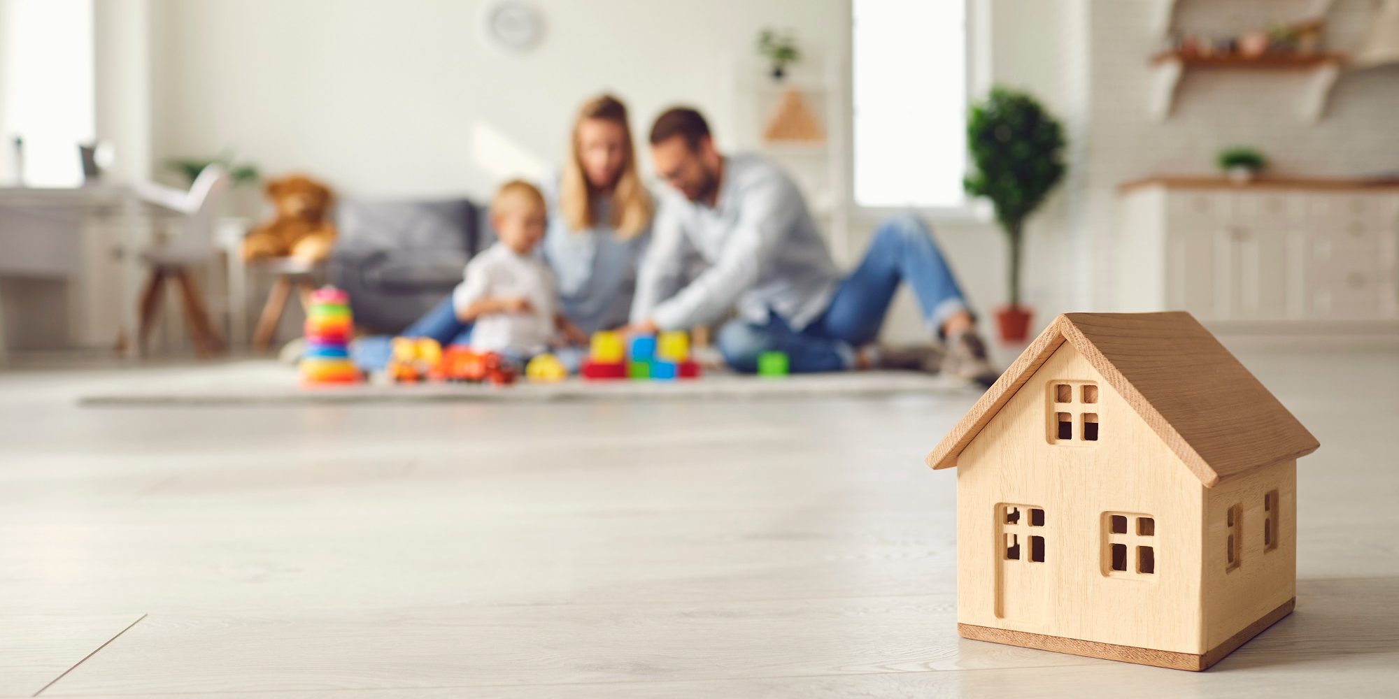 Close up of a small wooden house on the background of a young family with a child.