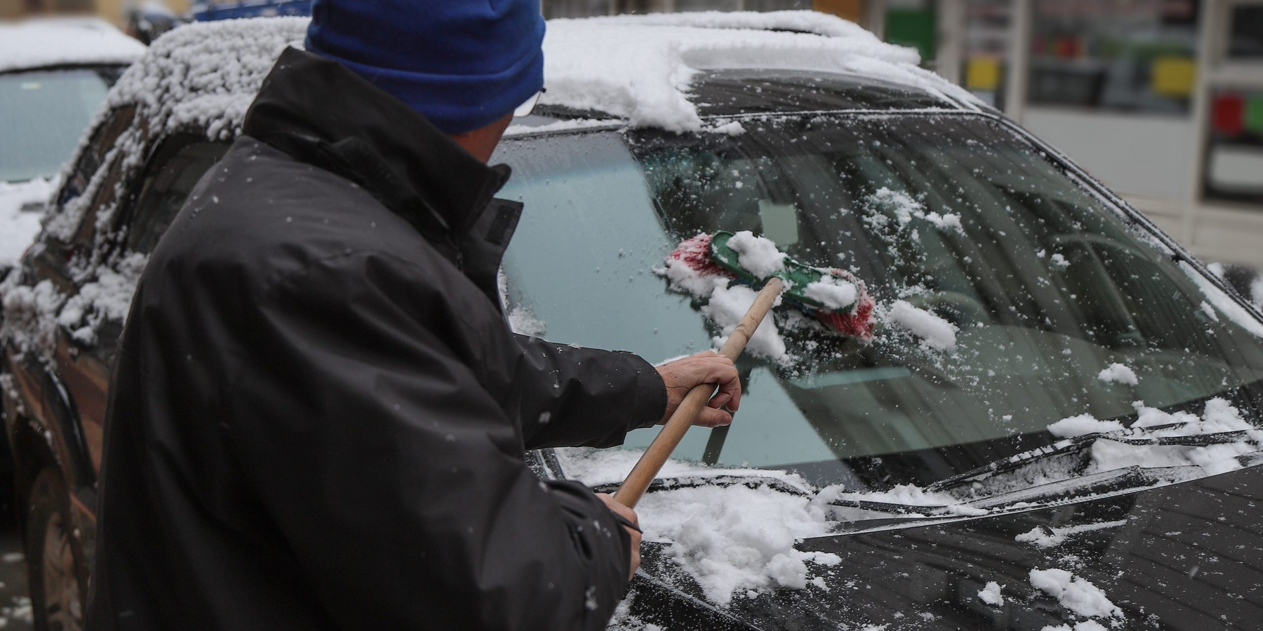 Man cleaning snow from car with brush.