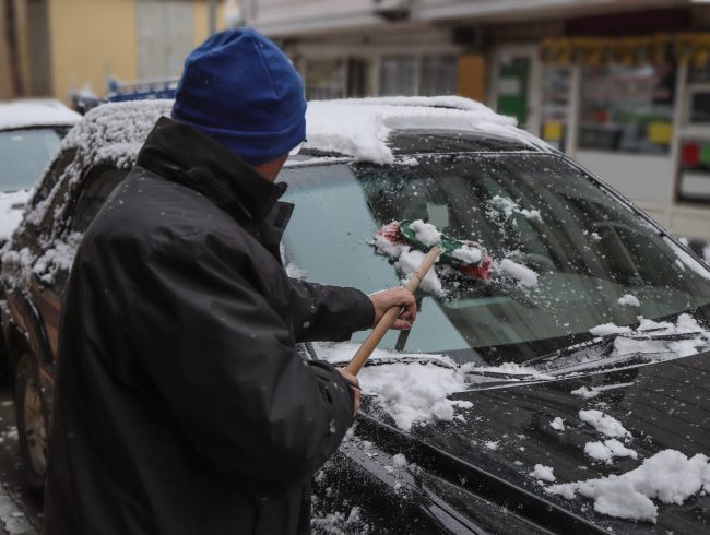 Man cleaning snow from car with brush.
