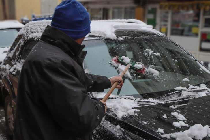 Man cleaning snow from car with brush.